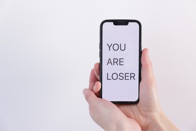 Photo of Cyber bullying. Woman holding smartphone with text You Are Loser on white background, closeup. Space for text