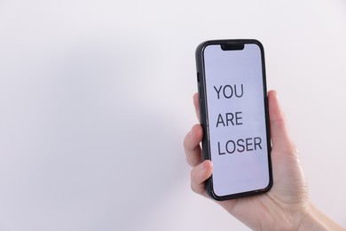 Photo of Cyber bullying. Woman holding smartphone with text You Are Loser on white background, closeup. Space for text