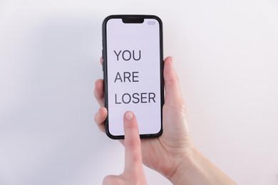 Photo of Cyber bullying. Woman holding smartphone with text You Are Loser on white background, closeup