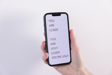 Photo of Cyber bullying. Woman holding smartphone with insults on light background, closeup