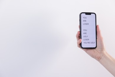 Photo of Cyber bullying. Woman holding smartphone with insults on light background, closeup. Space for text