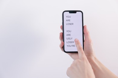 Photo of Cyber bullying. Woman holding smartphone with insults on light background, closeup. Space for text