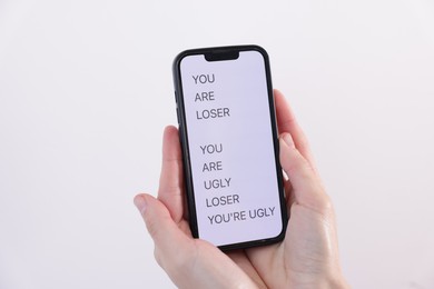 Photo of Cyber bullying. Woman holding smartphone with insults on light background, closeup