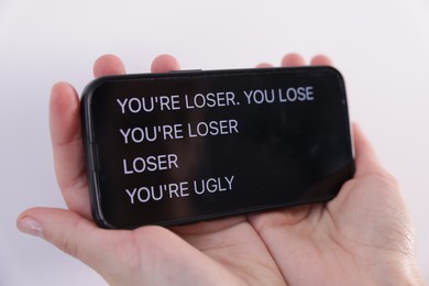 Photo of Cyber bullying. Woman holding smartphone with insults on white background, closeup