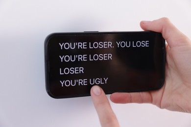 Photo of Cyber bullying. Woman holding smartphone with insults on white background, closeup