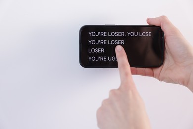 Photo of Cyber bullying. Woman holding smartphone with insults on white background, closeup. Space for text