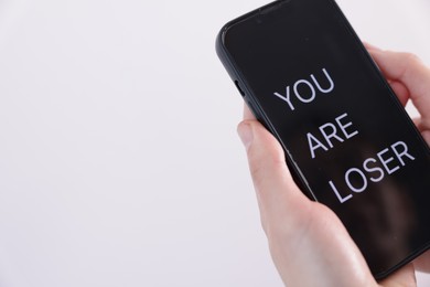 Photo of Cyber bullying. Woman holding smartphone with text You Are Loser on white background, closeup. Space for text