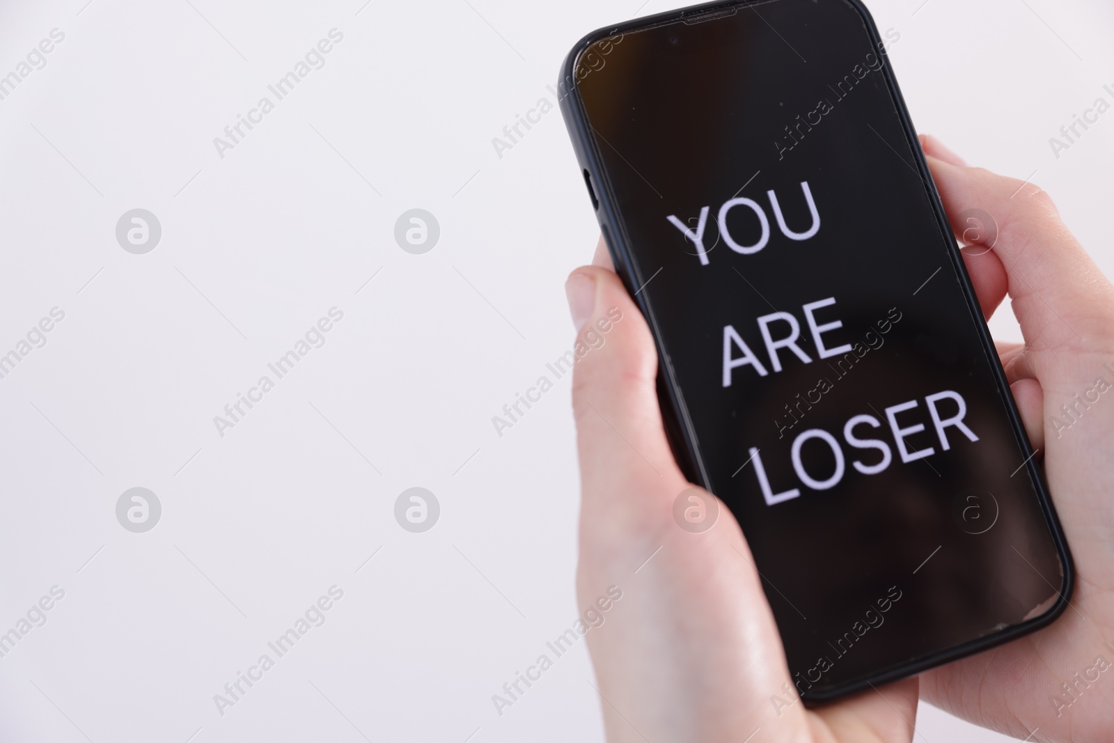 Cyber bullying. Woman holding smartphone with text You Are Loser on white background, closeup. Space for text Photo of Cyber bullying. Woman holding smartphone with text You Are Loser on white background, closeup. Space for text