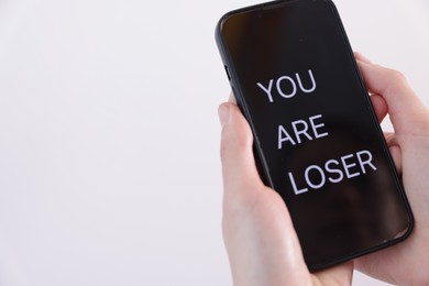 Photo of Cyber bullying. Woman holding smartphone with text You Are Loser on white background, closeup. Space for text