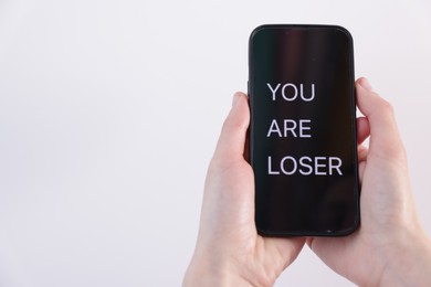Photo of Cyber bullying. Woman holding smartphone with text You Are Loser on white background, closeup. Space for text