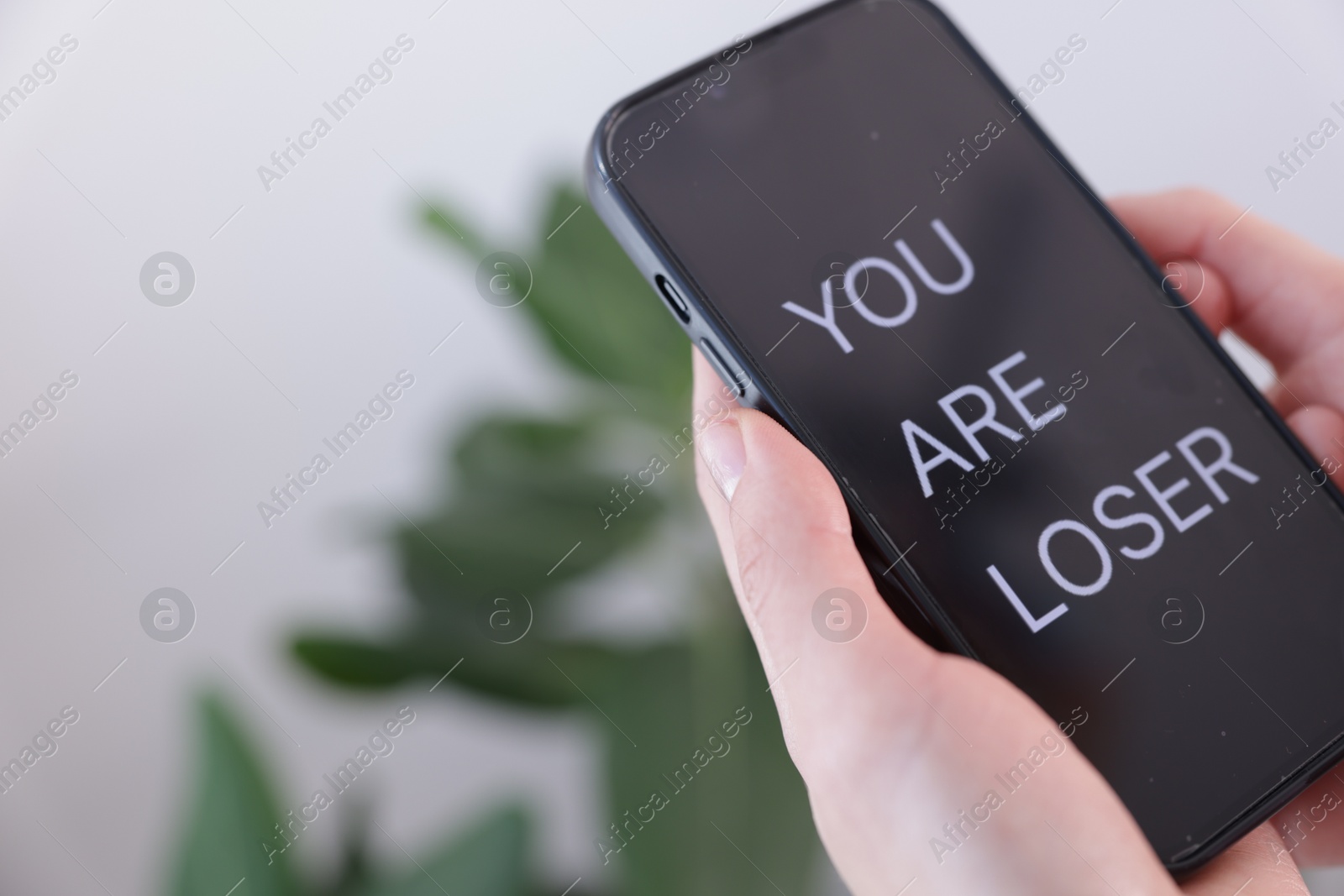 Cyber bullying. Woman holding smartphone with text You Are Loser on blurred background, closeup. Space for text Photo of Cyber bullying. Woman holding smartphone with text You Are Loser on blurred background, closeup. Space for text