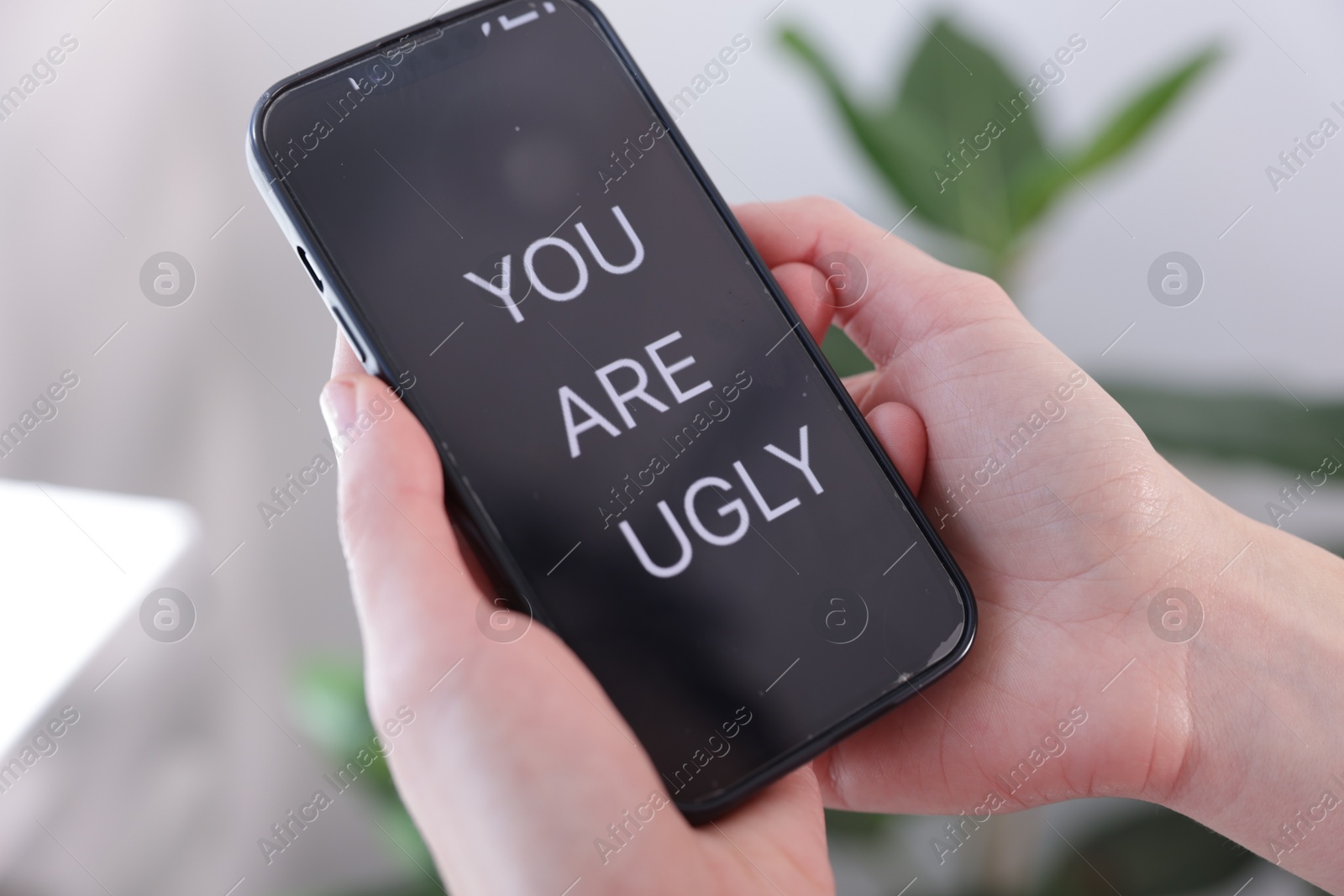 Cyber bullying. Woman holding smartphone with text You Are Ugly on blurred background, closeup Photo of Cyber bullying. Woman holding smartphone with text You Are Ugly on blurred background, closeup