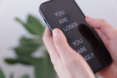 Photo of Cyber bullying. Woman holding smartphone with insults on blurred background, closeup