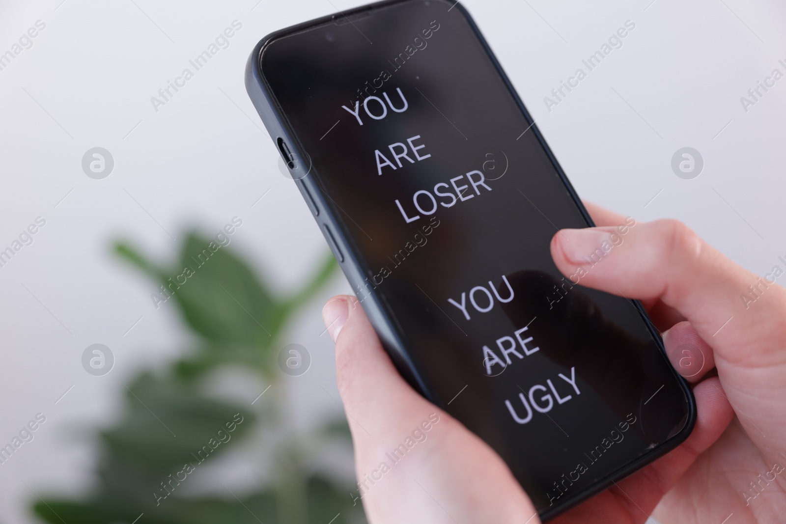 Cyber bullying. Woman holding smartphone with insults on blurred background, closeup Photo of Cyber bullying. Woman holding smartphone with insults on blurred background, closeup