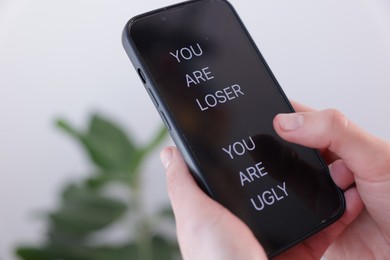 Photo of Cyber bullying. Woman holding smartphone with insults on blurred background, closeup