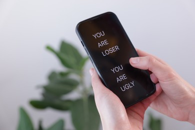 Photo of Cyber bullying. Woman holding smartphone with insults on blurred background, closeup. Space for text