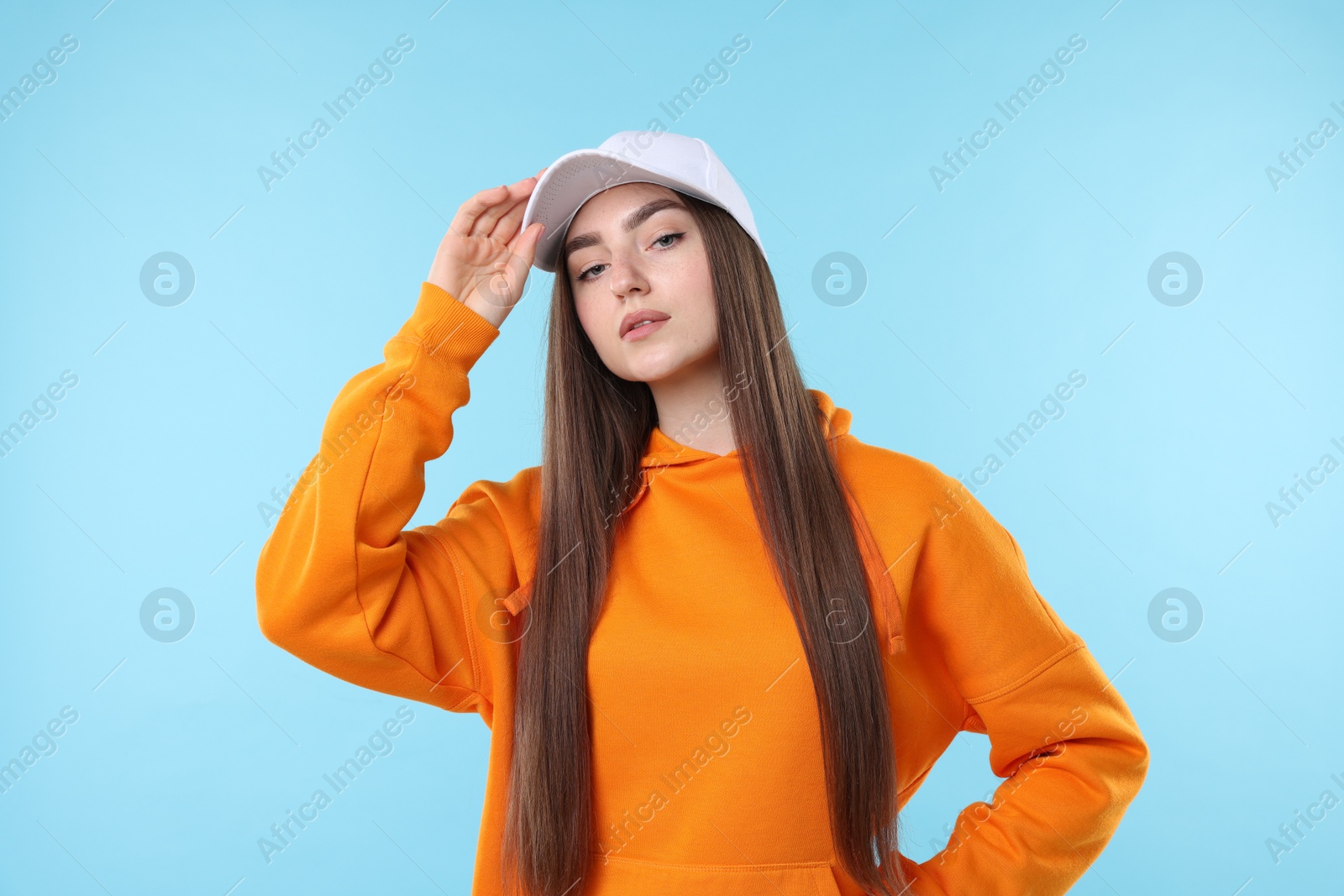 Portrait of beautiful woman in stylish baseball hat on light blue background Photo of Portrait of beautiful woman in stylish baseball hat on light blue background