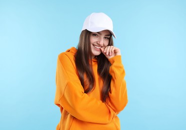 Photo of Portrait of smiling woman in stylish baseball hat on light blue background