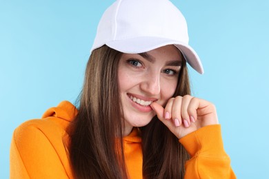 Photo of Portrait of smiling woman in stylish baseball hat on light blue background, closeup