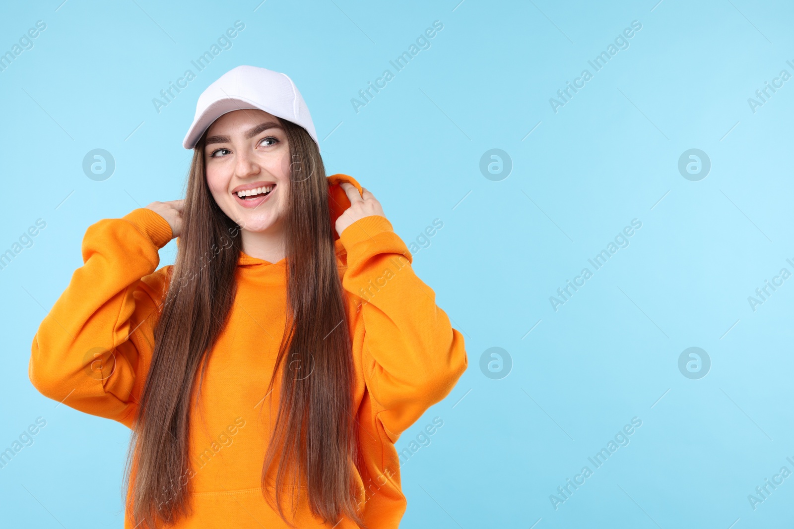 Smiling woman in stylish baseball hat on light blue background. Space for text Photo of Smiling woman in stylish baseball hat on light blue background. Space for text