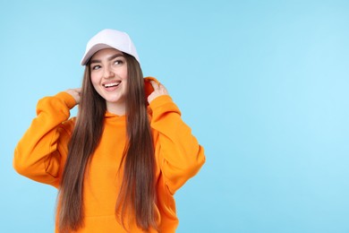 Photo of Smiling woman in stylish baseball hat on light blue background. Space for text