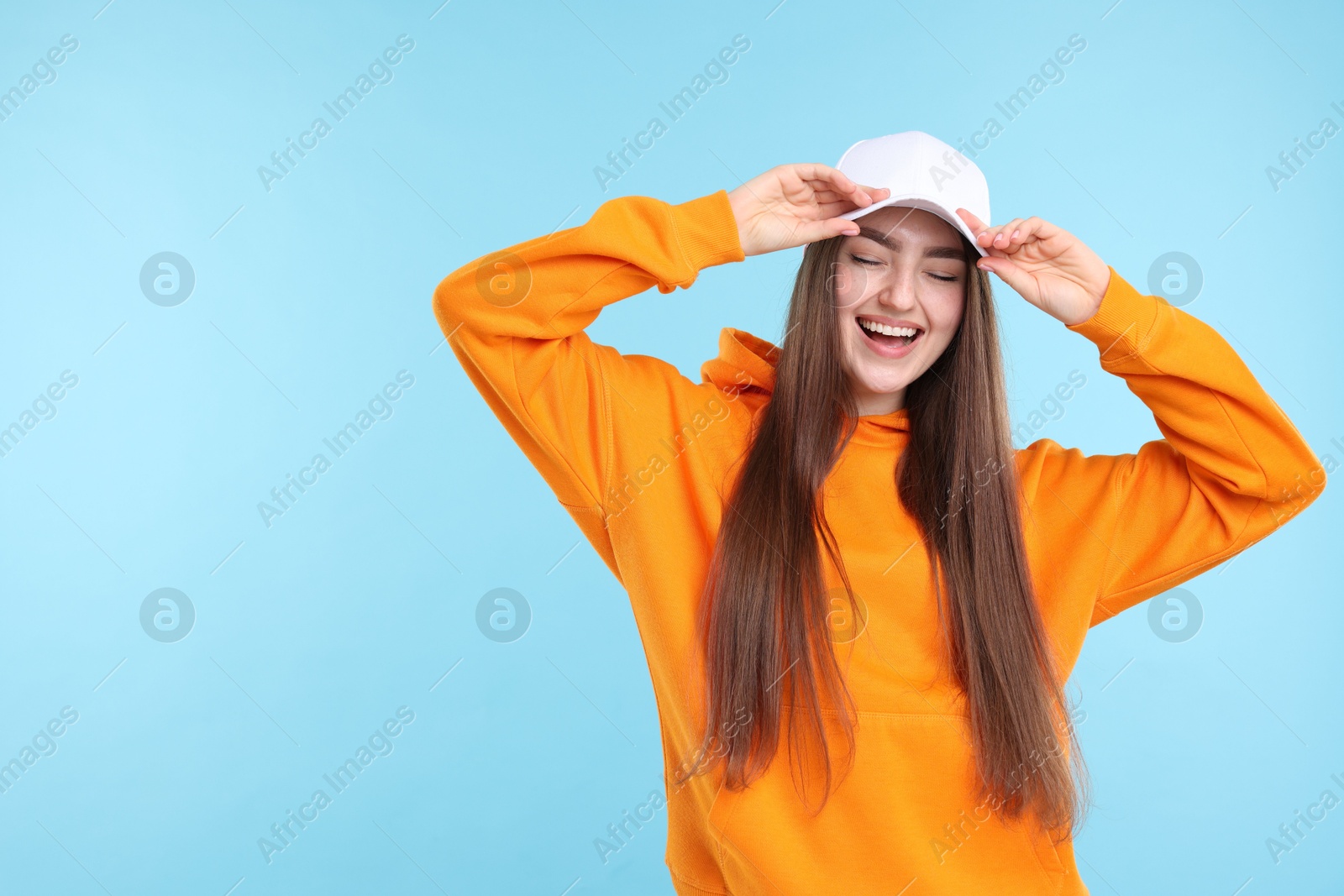 Smiling woman in stylish baseball hat on light blue background. Space for text Photo of Smiling woman in stylish baseball hat on light blue background. Space for text