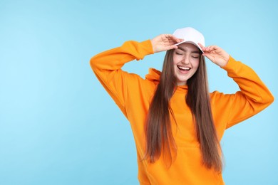 Photo of Smiling woman in stylish baseball hat on light blue background. Space for text