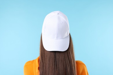 Photo of Woman in stylish baseball hat on light blue background, back view
