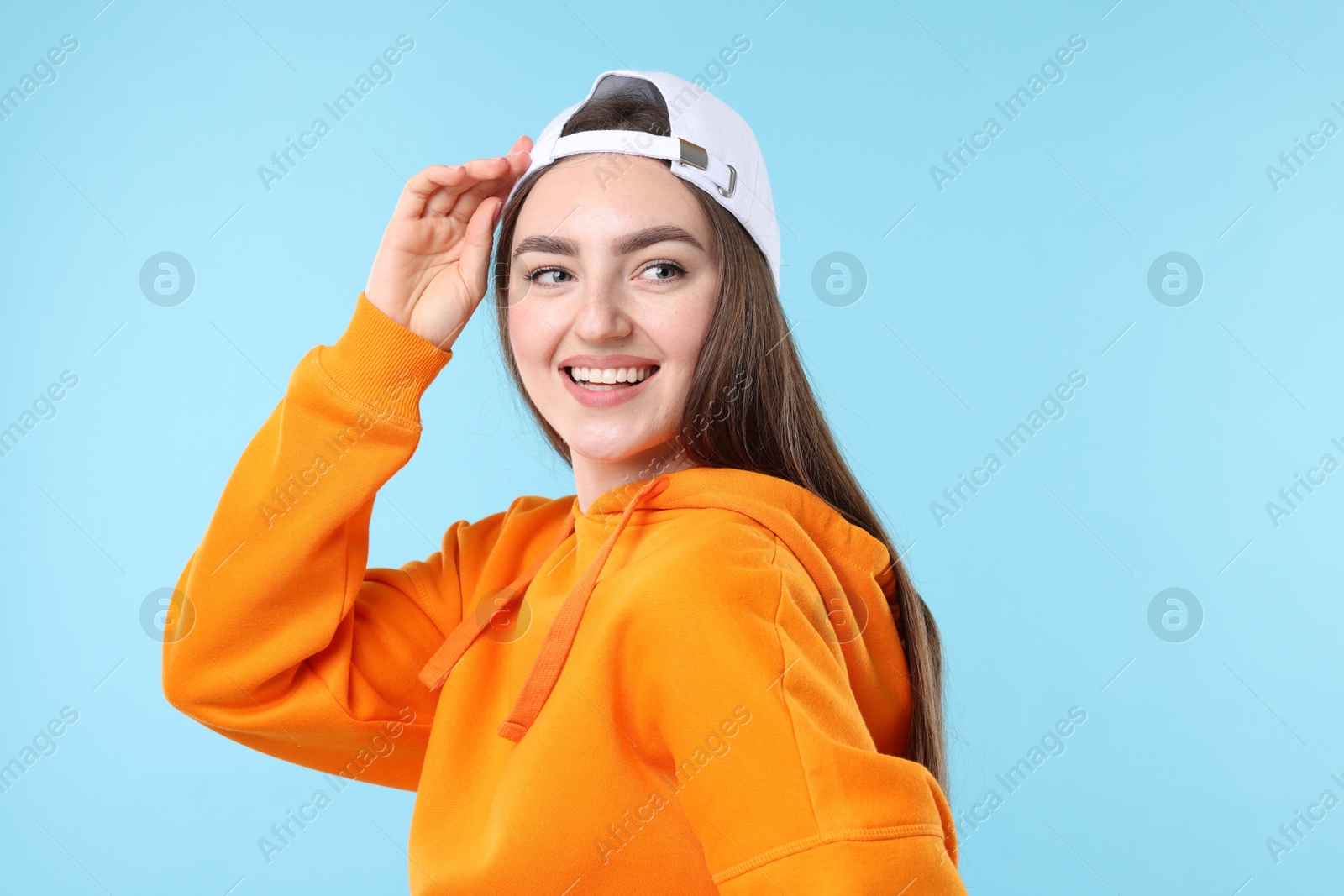 Smiling woman in stylish baseball hat on light blue background Photo of Smiling woman in stylish baseball hat on light blue background