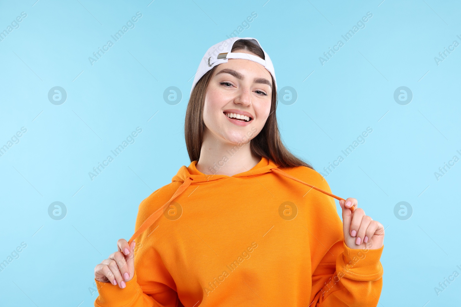 Smiling woman in stylish baseball hat on light blue background Photo of Smiling woman in stylish baseball hat on light blue background