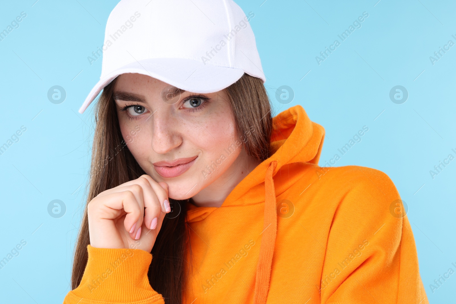 Portrait of beautiful woman in stylish baseball hat on light blue background, closeup Photo of Portrait of beautiful woman in stylish baseball hat on light blue background, closeup
