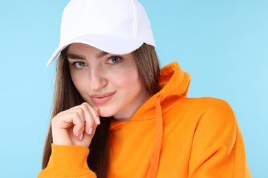 Photo of Portrait of beautiful woman in stylish baseball hat on light blue background, closeup