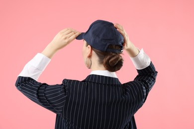 Photo of Woman in stylish baseball hat on pink background, back view