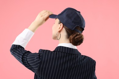 Photo of Woman in stylish baseball hat on pink background, back view