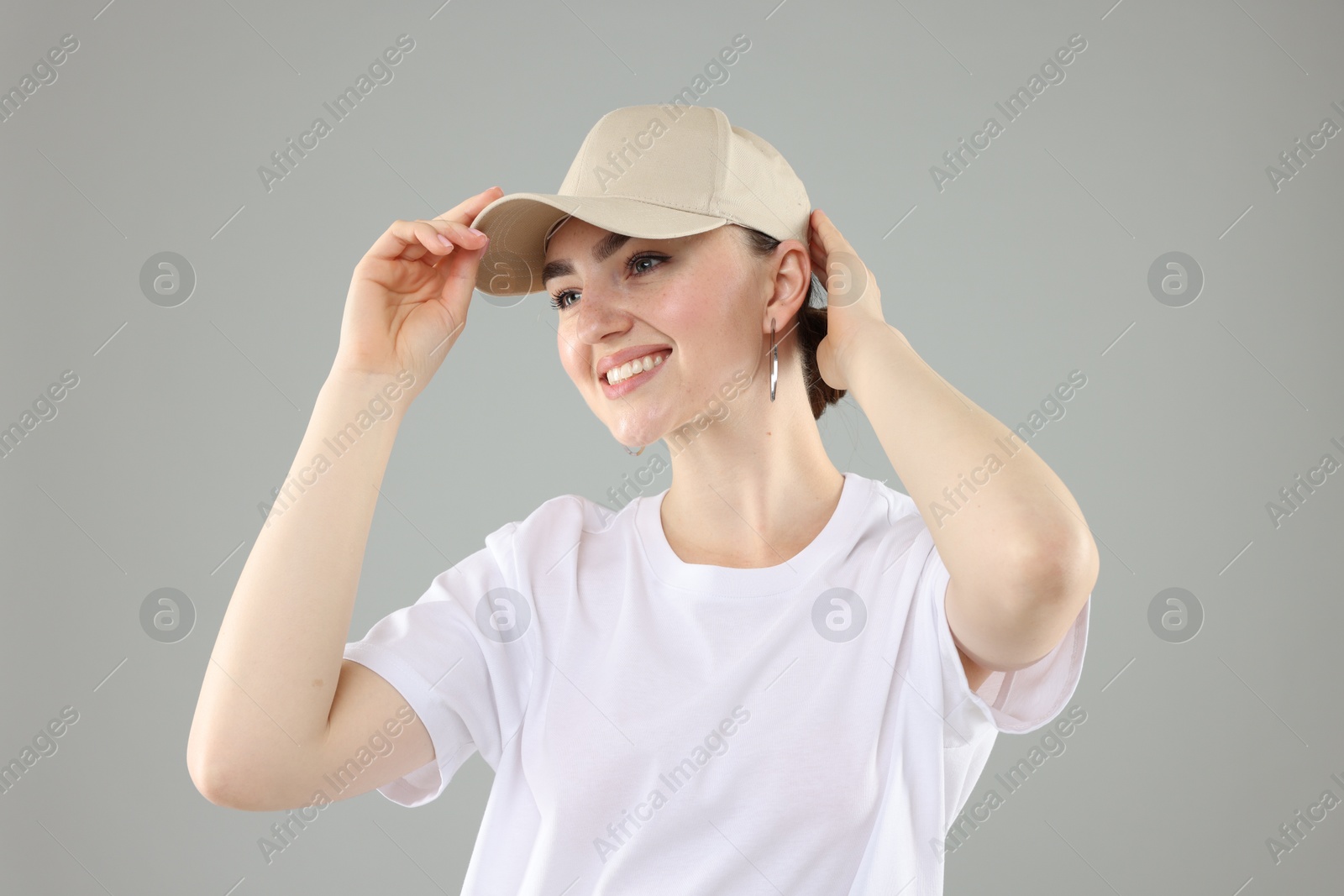 Smiling woman in stylish baseball hat on grey background Photo of Smiling woman in stylish baseball hat on grey background