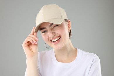 Photo of Smiling woman in stylish baseball hat on grey background, closeup