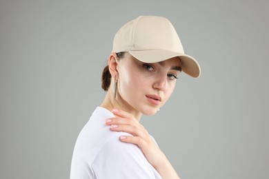 Photo of Beautiful woman in stylish baseball hat on grey background, closeup