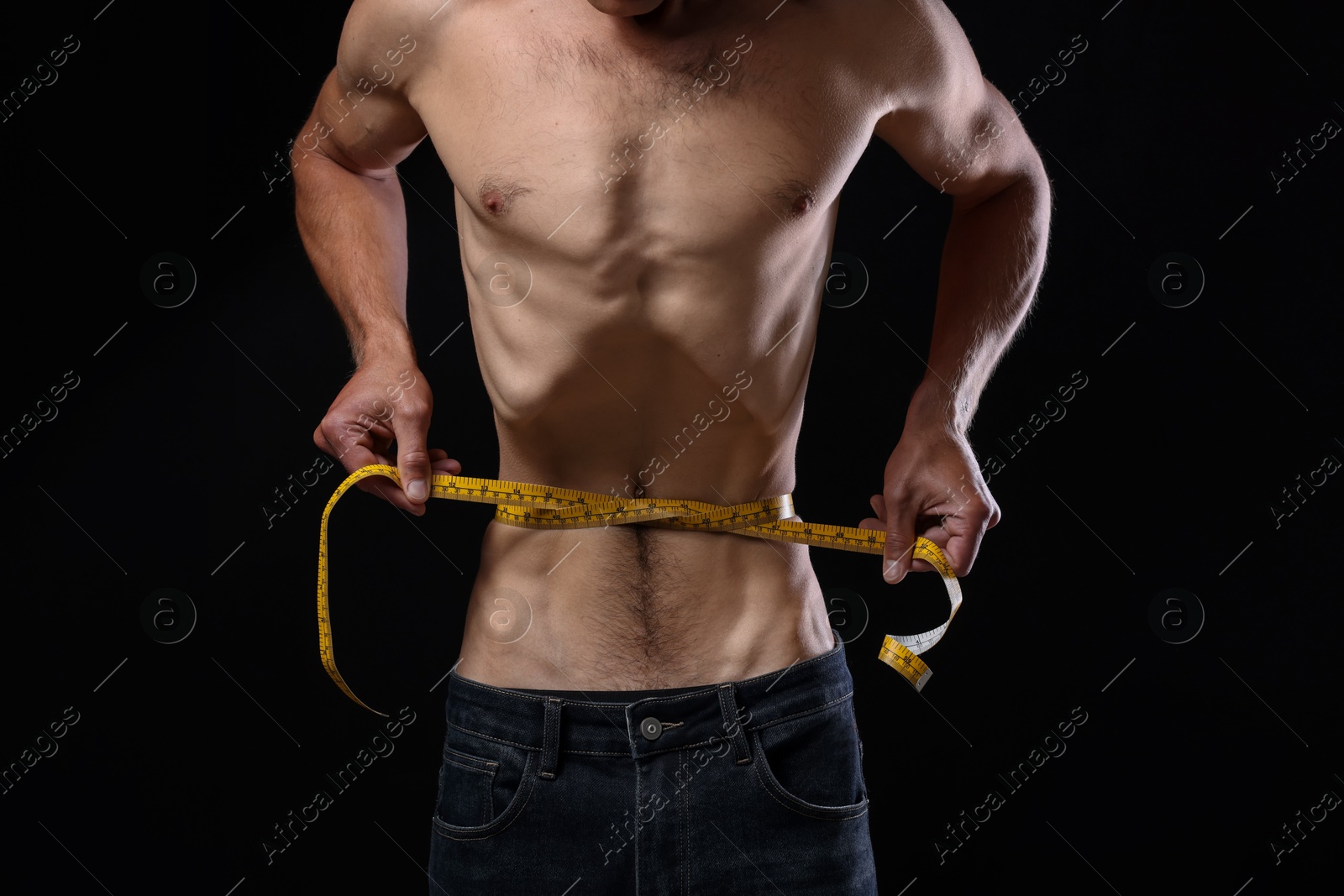 Anorexic man measuring his waist on black background, closeup Photo of Anorexic man measuring his waist on black background, closeup