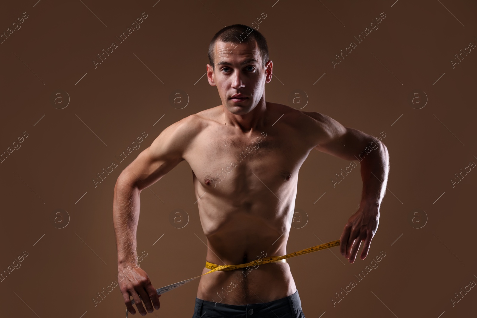 Anorexic man measuring his waist on beige background Photo of Anorexic man measuring his waist on beige background