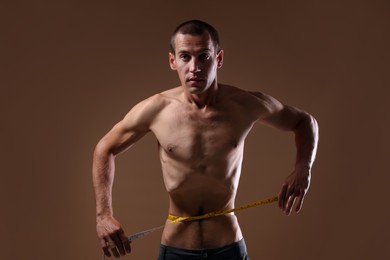 Photo of Anorexic man measuring his waist on beige background