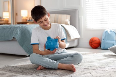 Photo of Boy putting pocket money into piggybank at home