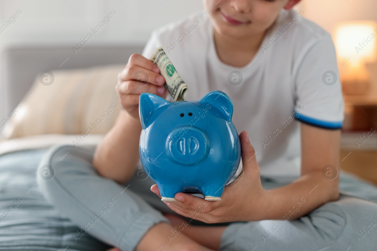 Boy putting pocket money into piggybank on bed at home, closeup Photo of Boy putting pocket money into piggybank on bed at home, closeup