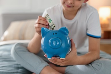 Photo of Boy putting pocket money into piggybank on bed at home, closeup