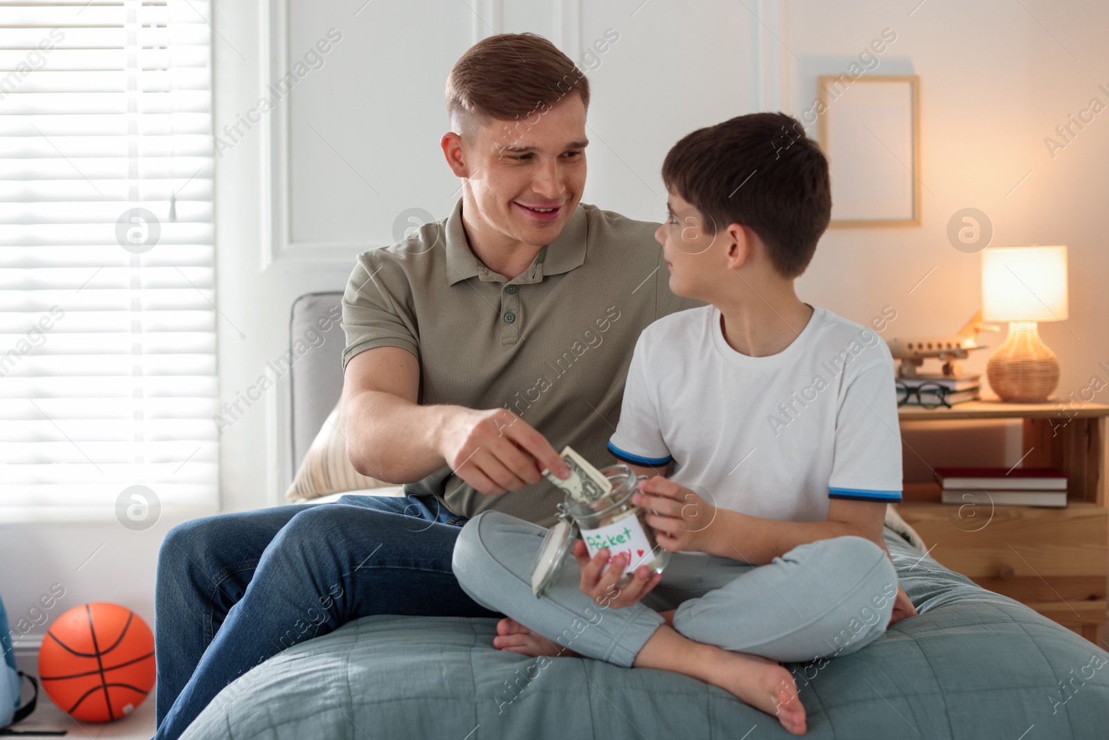 Father and son putting pocket money into jar on bed at home Photo of Father and son putting pocket money into jar on bed at home