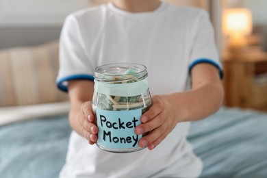 Photo of Boy with jar of pocket money on bed at home, closeup