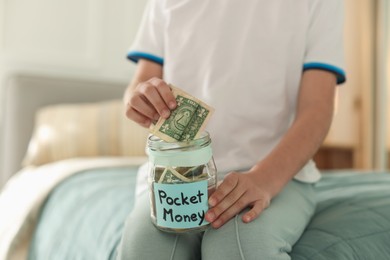 Photo of Boy putting pocket money into jar on bed at home, closeup
