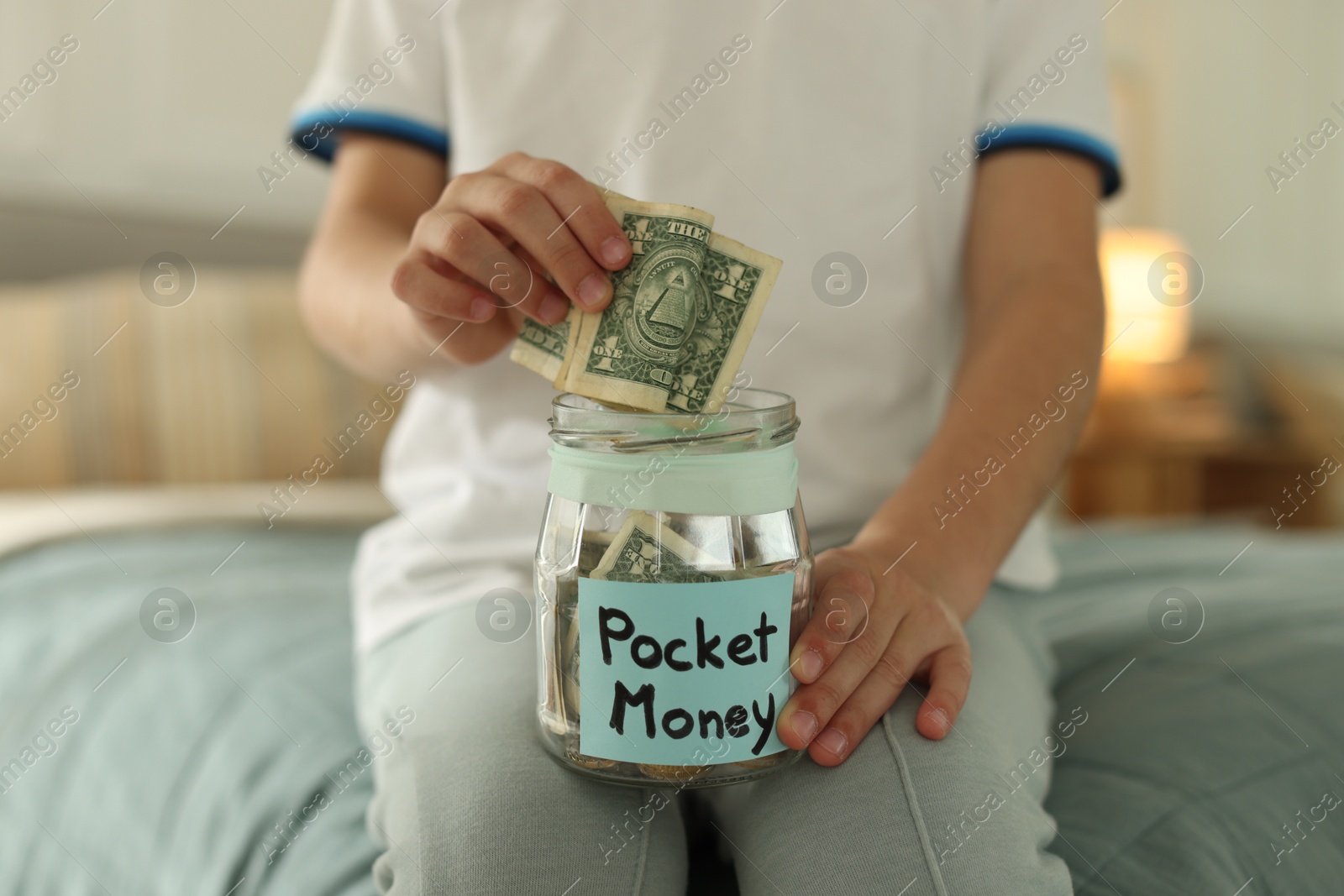 Photo of Boy putting pocket money into jar on bed at home, closeup