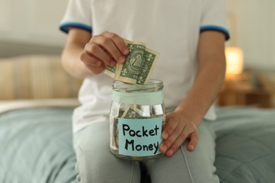 Photo of Boy putting pocket money into jar on bed at home, closeup