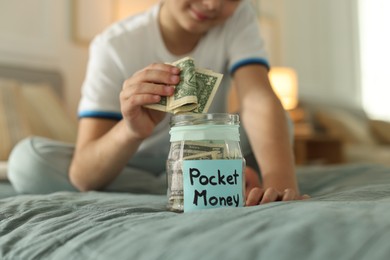 Photo of Boy putting pocket money into jar on bed at home, closeup