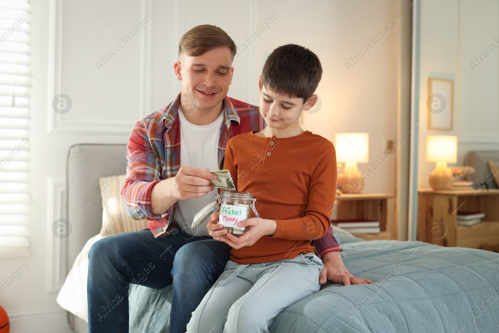 Father and son putting pocket money into jar at home Photo of Father and son putting pocket money into jar at home